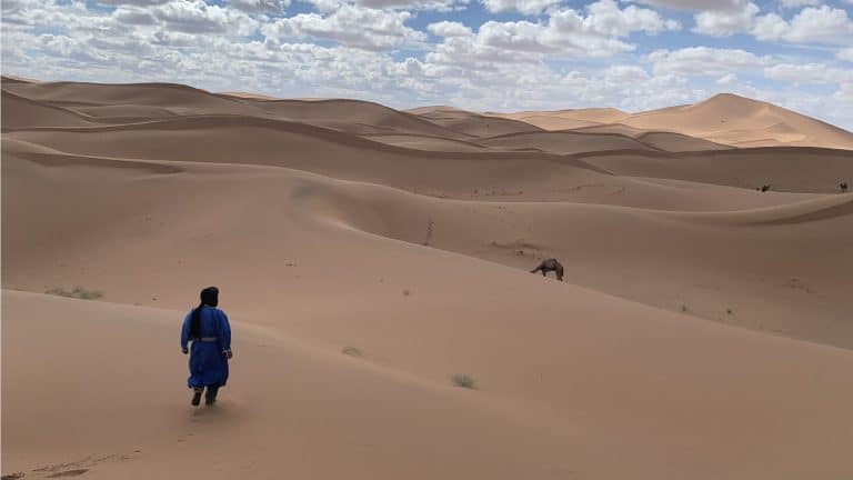 Un nomade marche dans les dunes vers son dromadaire.