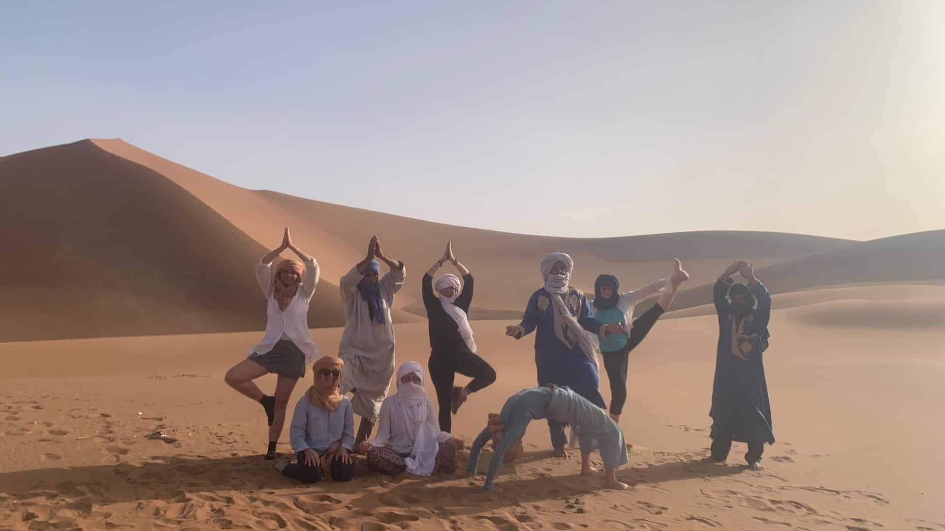 Un groupe pose en faisant des pratiques de Yoga devant une grande dune